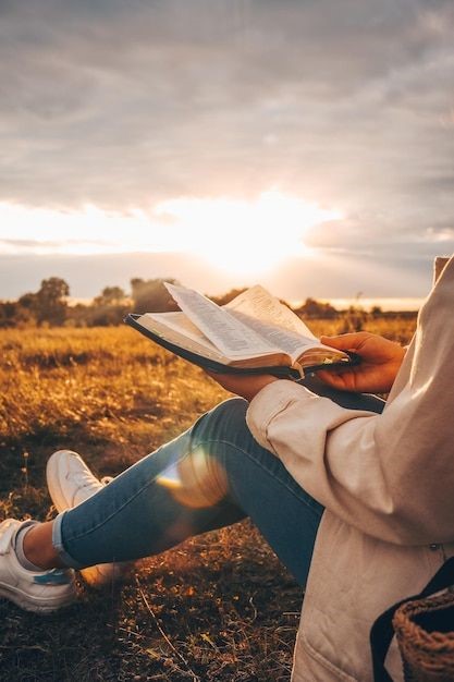 Mulher sentada em um campo com um livro na mão.